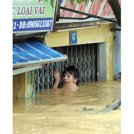 Một thiếu niên bám vào cửa nhà để đi trong biển nước ngập gần tới đầu.